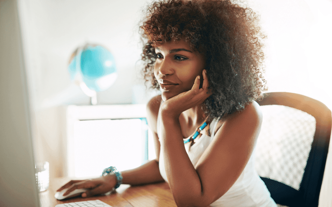 Black woman smiling and looking at computer screen with her hand on the mouse.